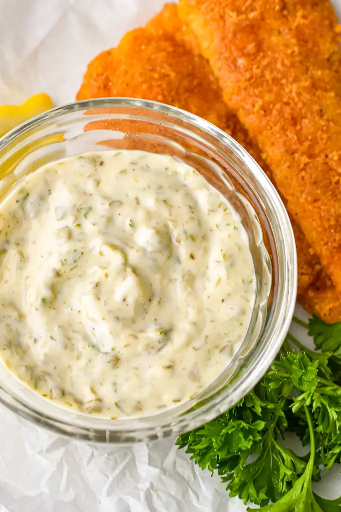 close up shot of low fodmap tartar sauce next to breaded fish, parsley and lemon on crinkled parchment paper