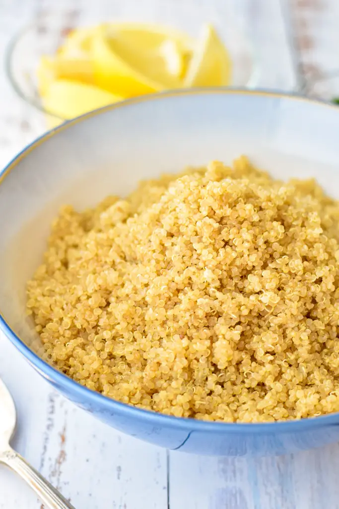 side angle of cooked, white quinoa in a blue bowl in front of a bowl of lemon slices